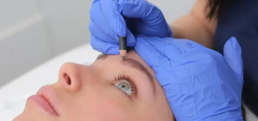 microblading φρυδιών με μολύβι από αισθητικό με μπλε γάντια
